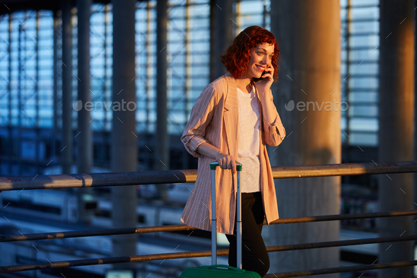 Smiling young woman talking on phone at station - Stock Photo - Images