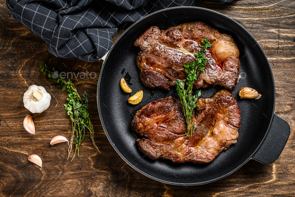 Grilled marble meat steaks Chuck eye roll in a pan. Dark wooden background. Top view