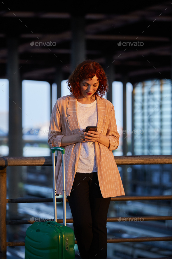 Smiling young woman browsing on phone at station - Stock Photo - Images