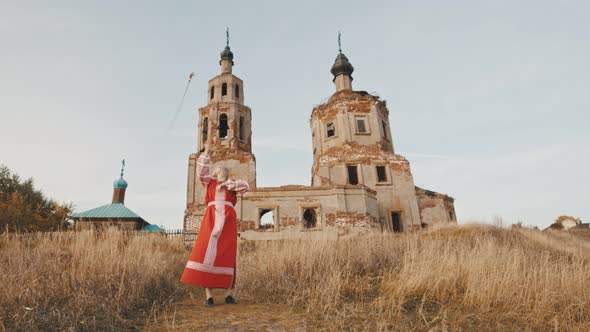 Woman in Red National Dress Wields Swords Against the Background of a Ruined Old Temple alt
