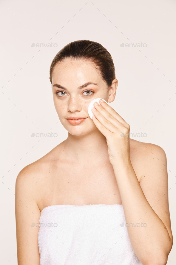 Peaceful female applying toner on radiant face with sponge