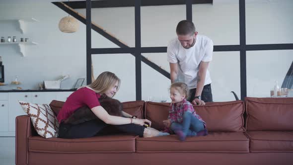 Portrait of Smiling Caucasian Man Admiring His Wife and Daughter Playing on Couch, Happy Blond Woman alt
