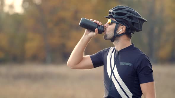 Cyclist In Helmet Relaxing After Workout Drinking Water. Fit Athlete Man Drinking Isotonic. alt
