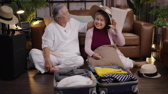 Elderly couple in Asia packs clothes in their luggage at home to prepare for their vacation. alt