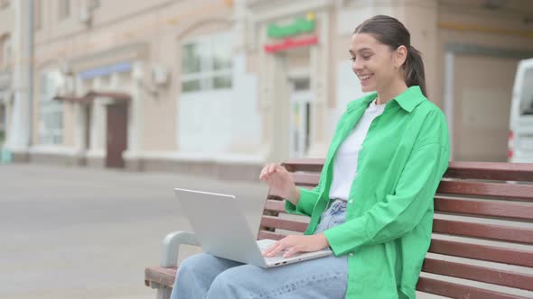 Hispanic Woman Talking on Video Call While Sitting Outdoor on Bench alt