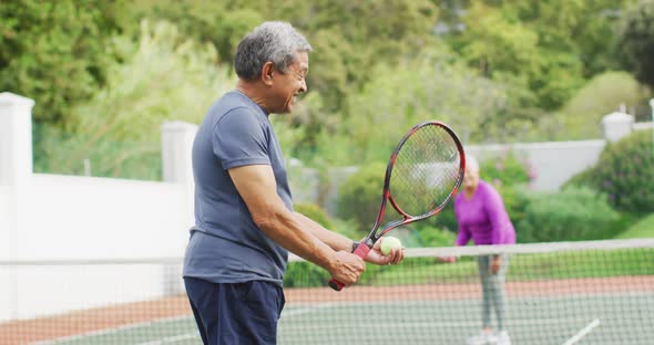 Video of happy biracial senior man holding racket and starting match on tennis court alt