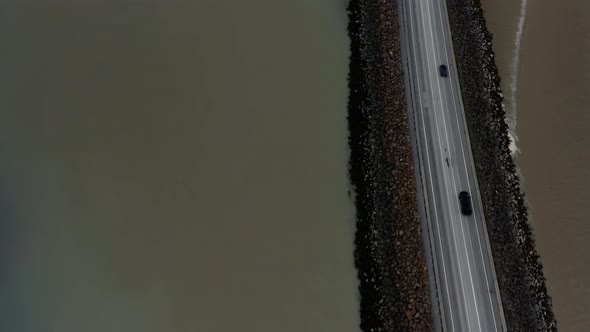 Vehicles Driving On The Road Between Shallow Murky River In Westfjord, Iceland. - aerial alt