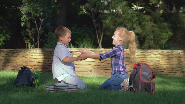 Educational Games, Scholar Girl and Boy Playing Clapping Game Sitting on Lawn After Schooling on alt