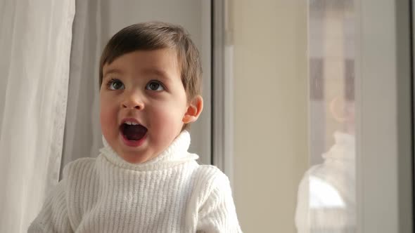 Baby Boy in White Knitted Sweater Sitting By the Window in Winter alt