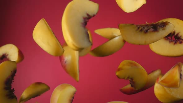 Slices of the Fresh Ripe Peach are Bouncing on the Wine Red Background alt