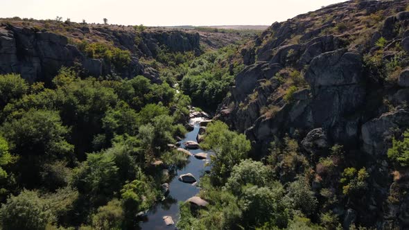 Drone Shot Over a Narrow Rocky Canyon with Trees and a Small River