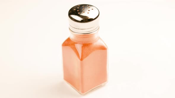 Glass Pepperjar with Stainless Steel Cap Full of Red Paprika Pepper Powder Spinning on White