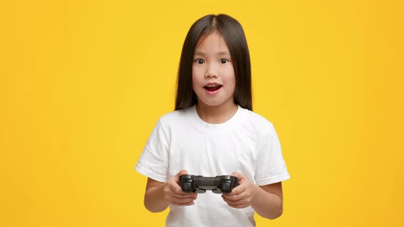 Asian Girl Playing Video Game Having Fun Over Yellow Background alt