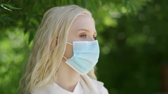 Young Blonde Woman in a Medical Mask Looks Tiredly Into the Distance