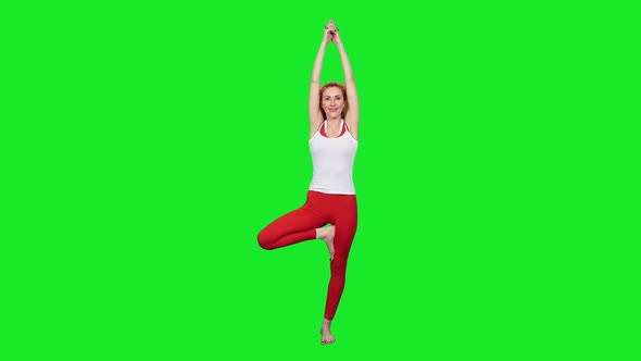 Fit Sporty Woman Standing On One Leg During Yoga Exercises Against Green Screen