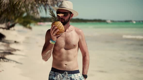 Guy Walking On Tropical Beach With Pineapple. Man Relaxing On Caribbean Beach. Tanned Man In Hat. alt