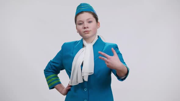 Confident Little Stewardess Putting Hand on Hip Stretching Palm Showing Aside Smiling Looking at alt