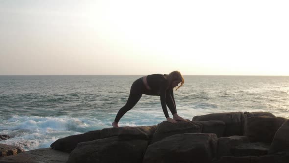 Young Woman with Long Hair Stretches on Grey Rocky Cliff alt