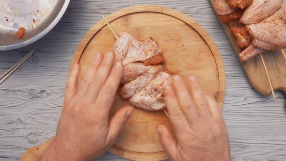 Top View of the Hands Piercing Raw Chicken Wings with a Wooden Skewer  alt
