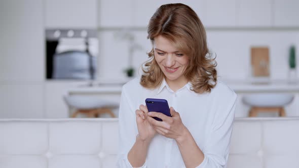 Cheerful Female Texting on Mobile in Apartment