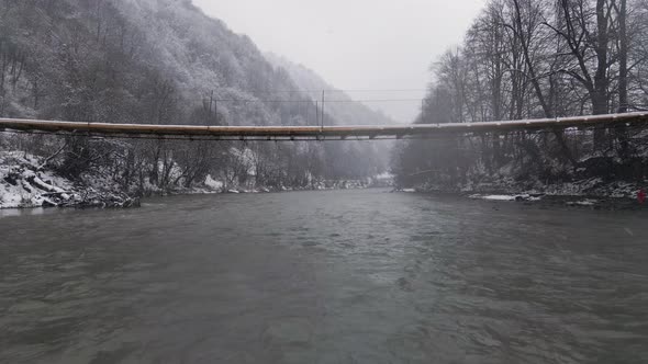 Drone View Flying Forward Over the River and Under the Cable Bridge in Blizzard Snowy Weather