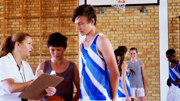 Female coach instructing schoolboys in basketball court alt