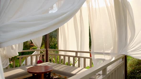 Outdoor wooden gazebo with white curtains.