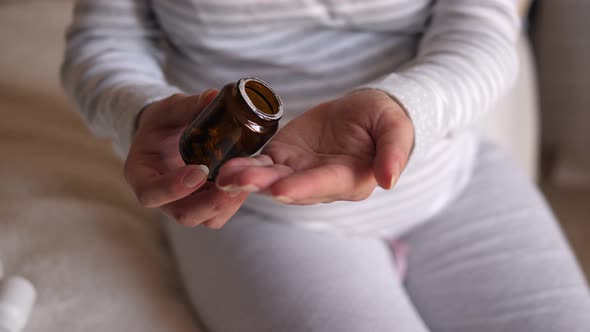 A Pregnant Woman Sits on the Bed and Pours Pills Into Her Hand. Close-up. alt