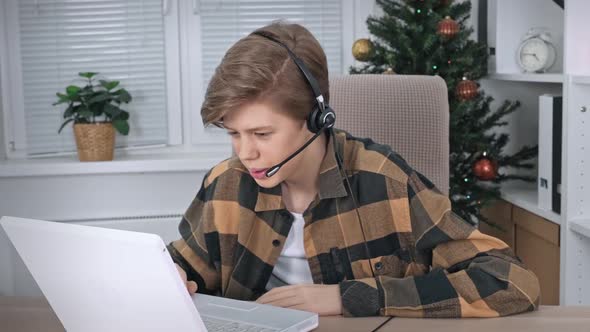 A Teenage Boy Wearing Headphones with a Laptop Talking on a Video Call Studying with a Teacher