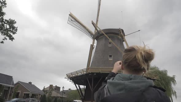 Panning Shot of a Young Woman Taking a Picture of an Old Dutch Windmill alt