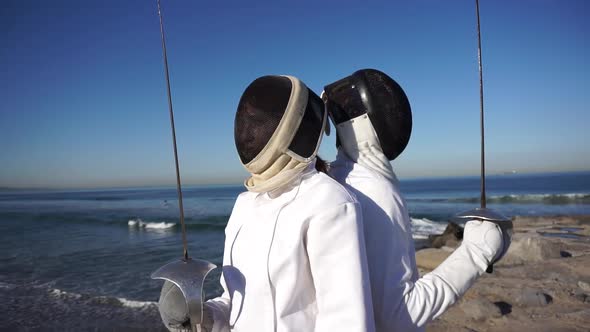 A man and woman fencing on the beach. alt
