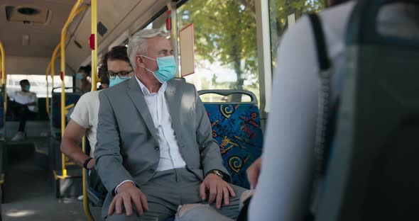 An Elderly Businessman in a Suit with Gray Hair and a Protective Mask Over Face alt