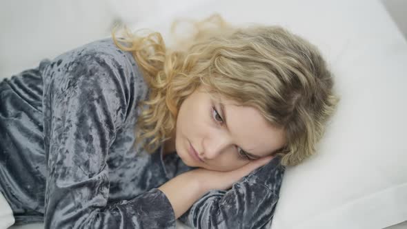 Closeup of Sad Beautiful Young Caucasian Woman Lying in White Bed Thinking alt