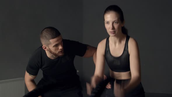 Young Woman with Instructor Using Battle Ropes in Gym