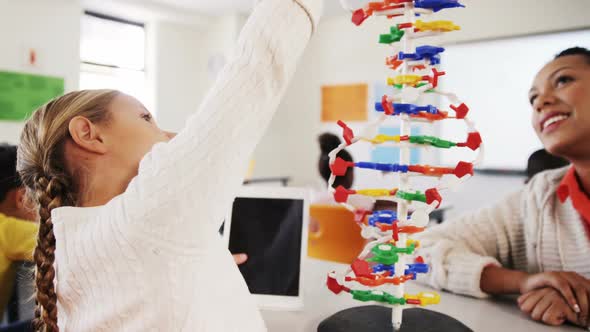 Teacher assisting schoolgirl with molecule model in classroom alt