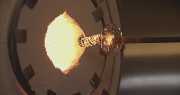Professional glassblower working the oven with a piece of glass design alt