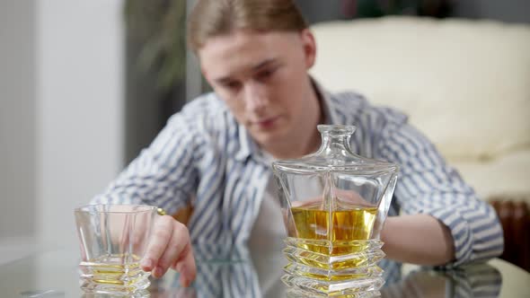 Blurred Sad Caucasian Man Moving Apart Glass and Decanter with Whiskey and Putting Head on Glass alt