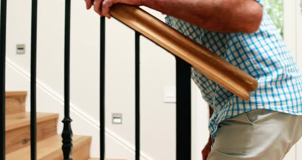 Senior man climbing upstairs with walking stick alt