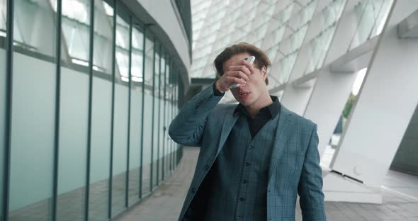 Shocked Businessman Looks Into a Smartphone and Takes Off His Glasses in Shock Standing Near an alt