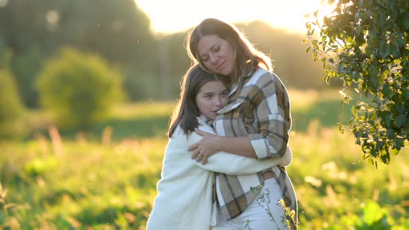 Loving tender mum hugging with a cute daughter on a field at sunset on a summer