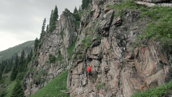 Man Athlette Climbing on the High Rock in the Mountains alt
