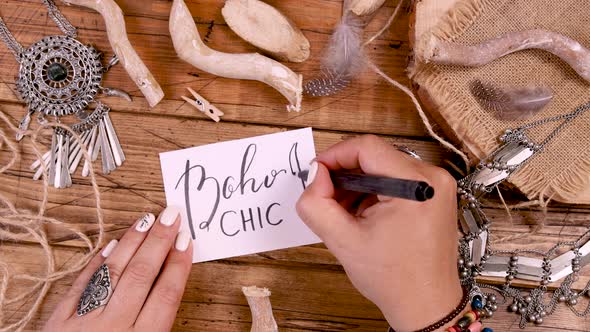 Hand drawing a feather on a boho card on a wooden table top view alt
