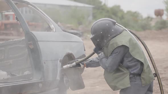 A man in a protective clothing and hard hat processes metal. Worker in sandblasting uniform alt