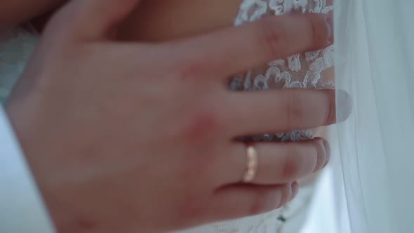 Groom Embraces the Bride Passes Her Hand Over Her Shoulders Closeup alt