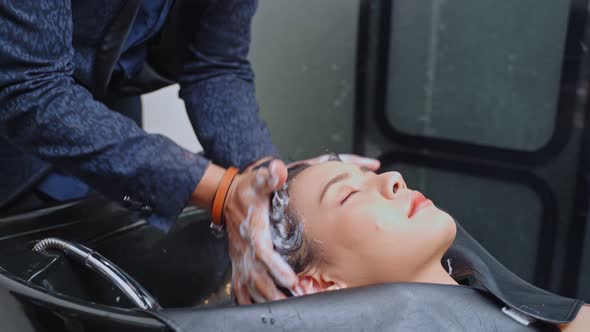 Asian young woman laying on salon washing bed getting hair washed in hair salon by stylist. alt