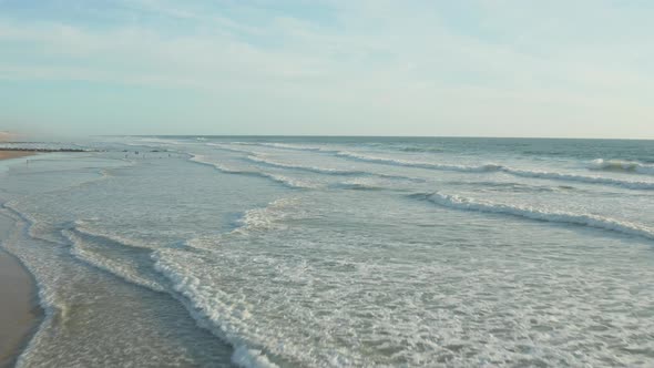Few Surfers on Empty Beach with Perfect Waves in Sunset Light and White Foam Waves, Aerial Forward alt