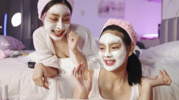 Beautiful young woman in white bathrobe applying a revitalizing  mask her friend's face alt