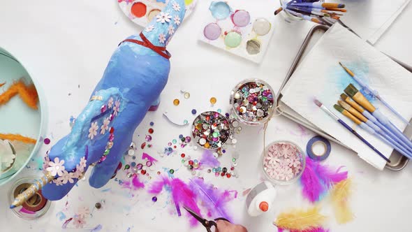 Step by step. Decorating painted paper mache unicorn with paper flowers and jewels. alt