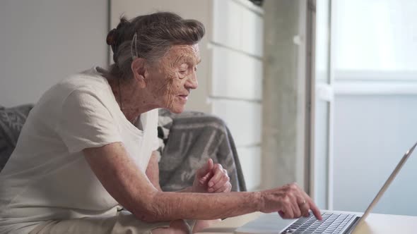 Elderly Woman Having a Video Call with Family, Smiling and Waving. Senior Woman with Gray Hair Make alt