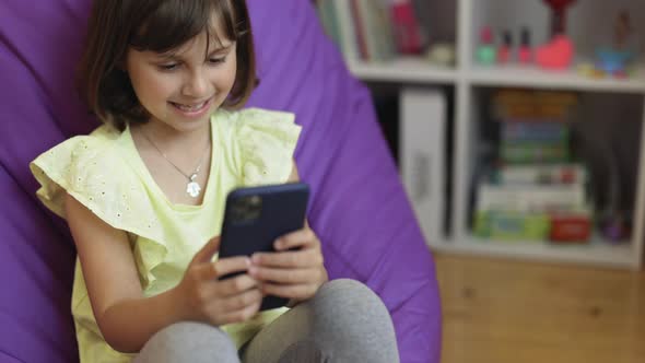 Cute Child Girl Holds Phone Using Smartphone Browsing Internet Uses Video Communication at Home